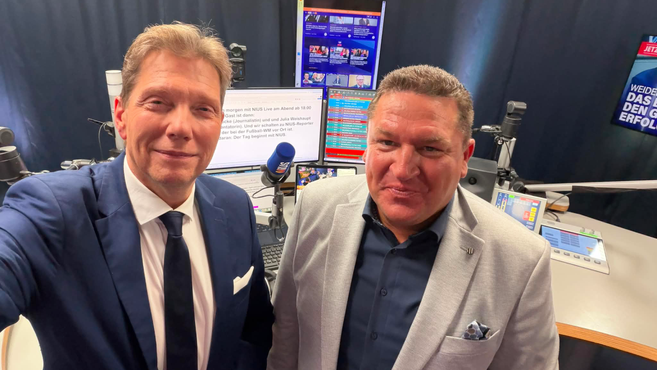 Moderator Andreas Dorfmann und Marcus Held gemeinsam im NIUS Studio während einer politischen Sendung zu Bundestagsdebatten, den Unruhen in Belfast und steigenden Spritpreisen in Deutschland.